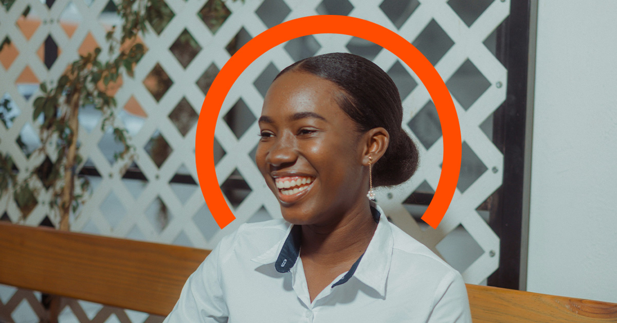A woman sits on a wooden bench, smiling, with an orange semicircle graphic behind her head and a white lattice background, embodying the positivity that comes from employee financial wellness.