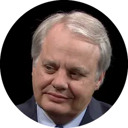 A person with grey hair and a suit is looking slightly to the side with a thoughtful expression.