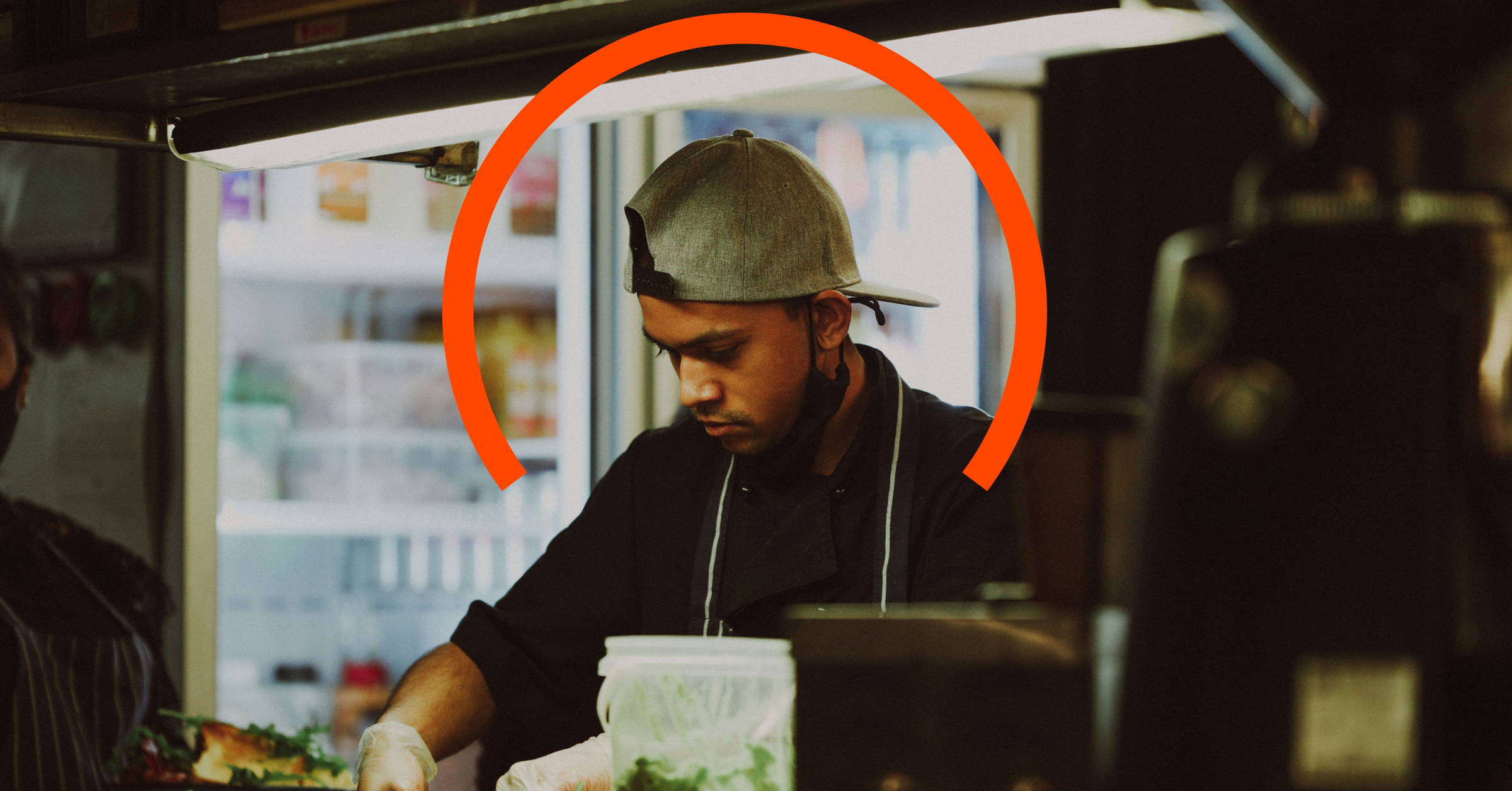 A person wearing a backwards cap and dark clothing prepares food in a kitchen, with an orange semicircle graphic added over their head.