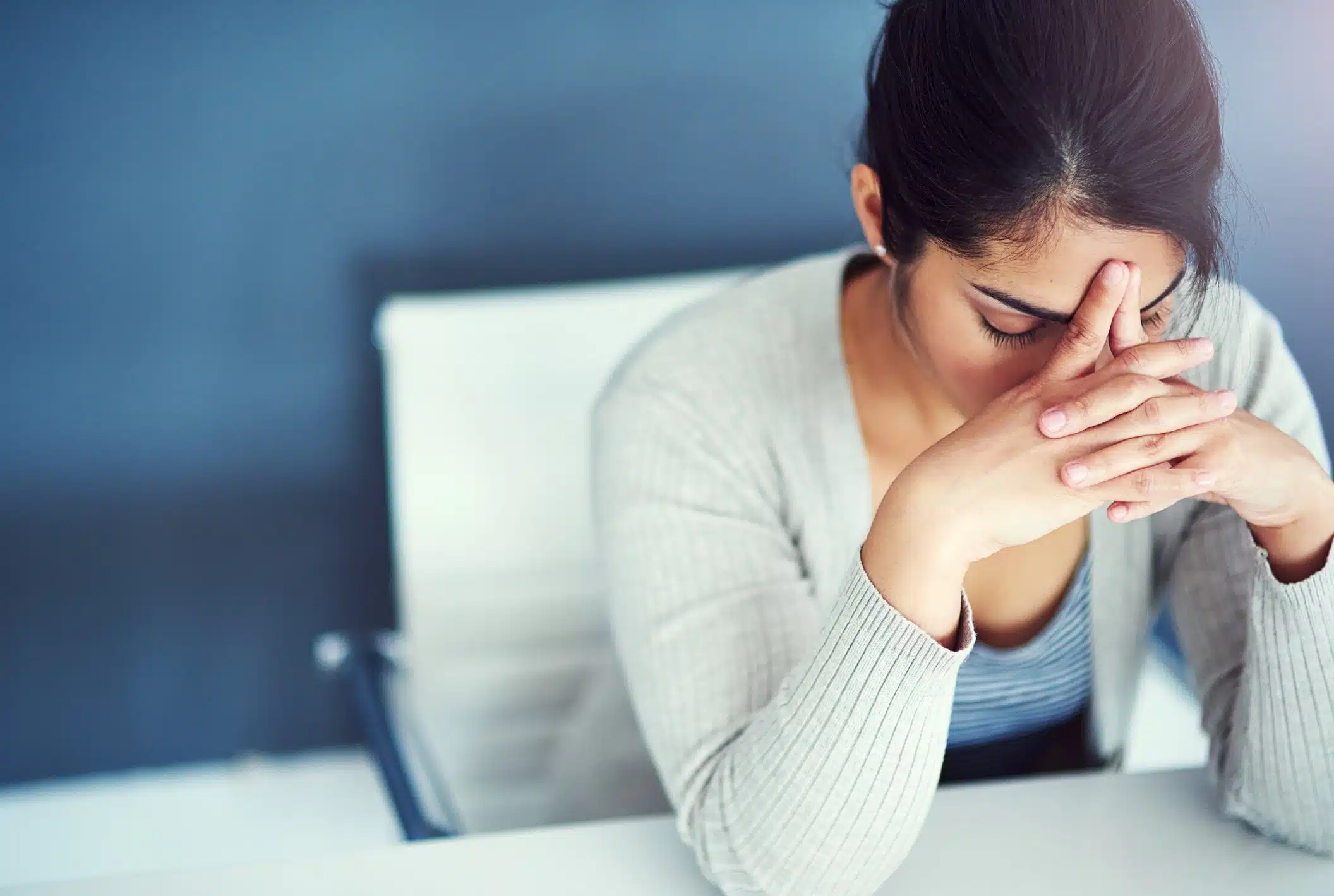 A person sits at a desk with their head resting on clasped hands, appearing stressed or deep in thought.