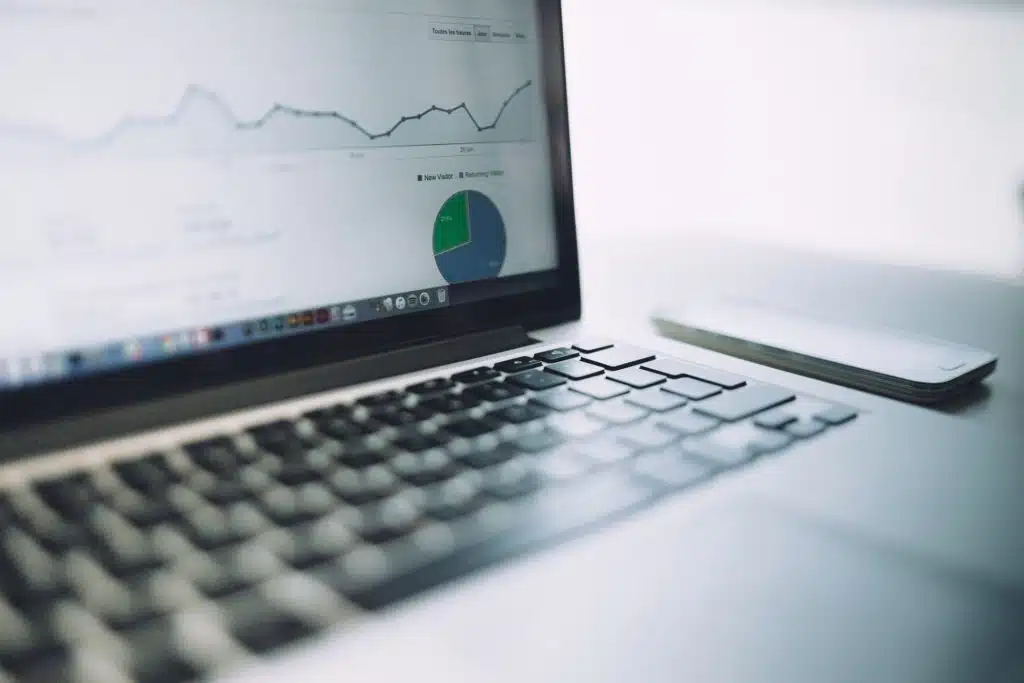 A laptop screen displaying graphs and a pie chart suggesting data analysis of employee absenteeism. A smartphone is placed next to the laptop on a white surface.
