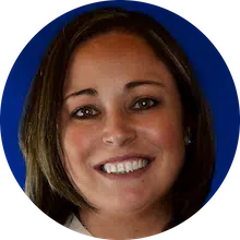 A woman with shoulder-length brown hair is smiling in front of a blue background.