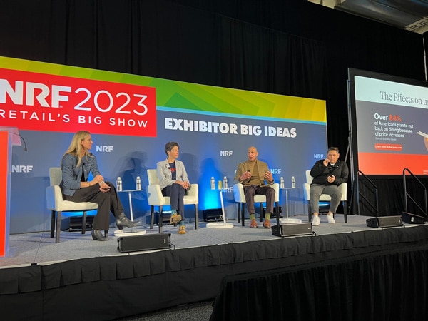 Four people are seated on a stage for a panel discussion at NRF 2023: Retail's Big Show. Behind them, a large banner reading "EXHIBITOR BIG IDEAS" is displayed. One panelist is speaking while the rest listen. A screen on the right shows a slide titled "The Effects on" with data on price increases.