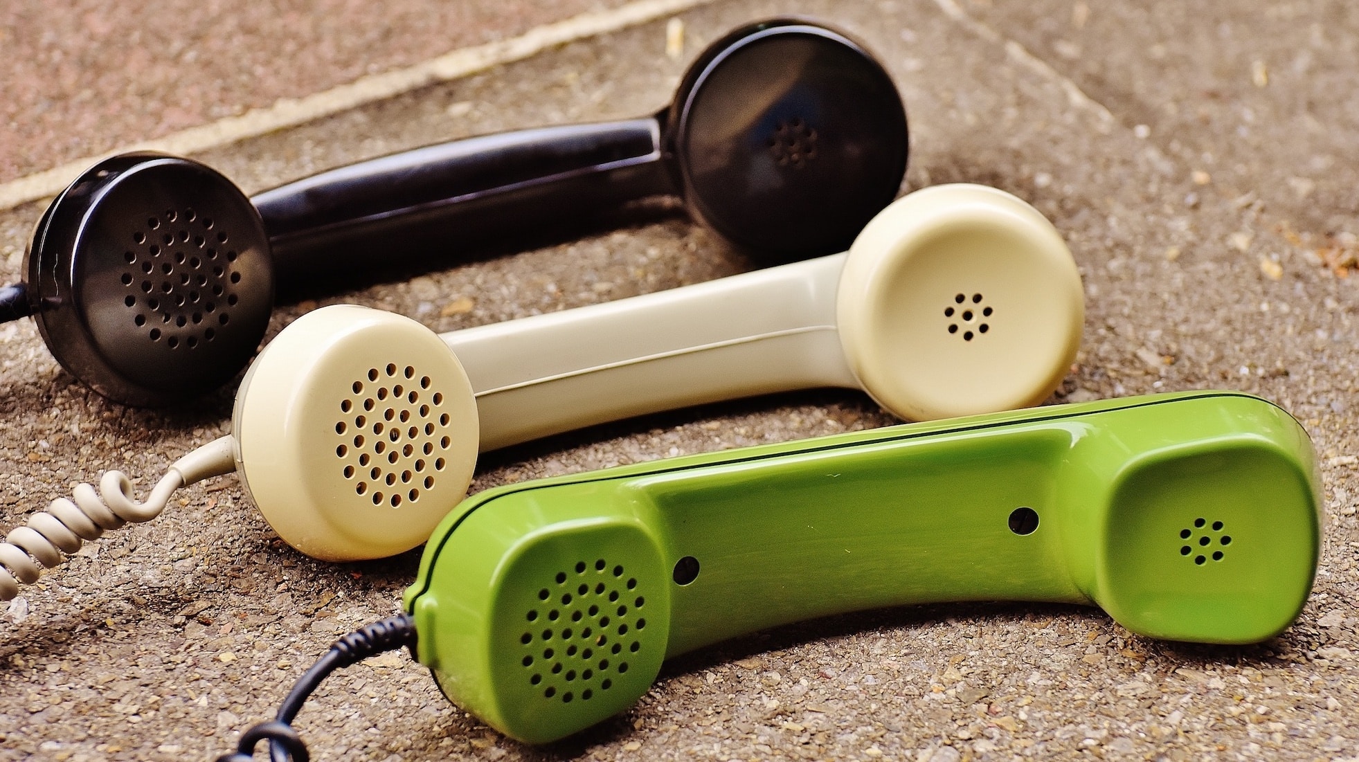 Three vintage telephone handsets in black, cream, and green lying on a pavement.