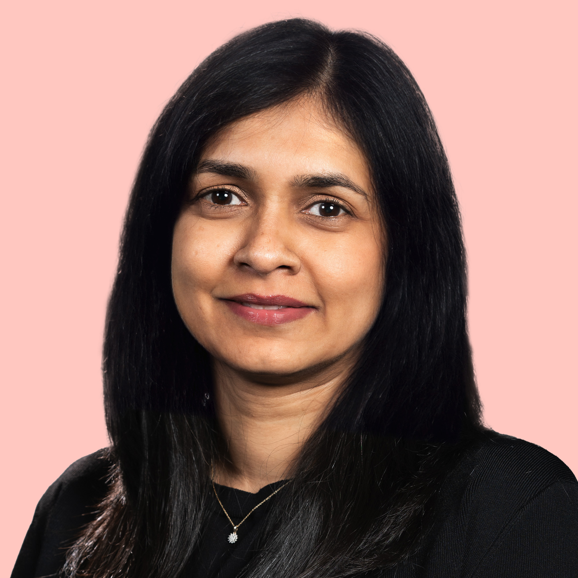 A person with long black hair is wearing a black top, posing against a light pink background.