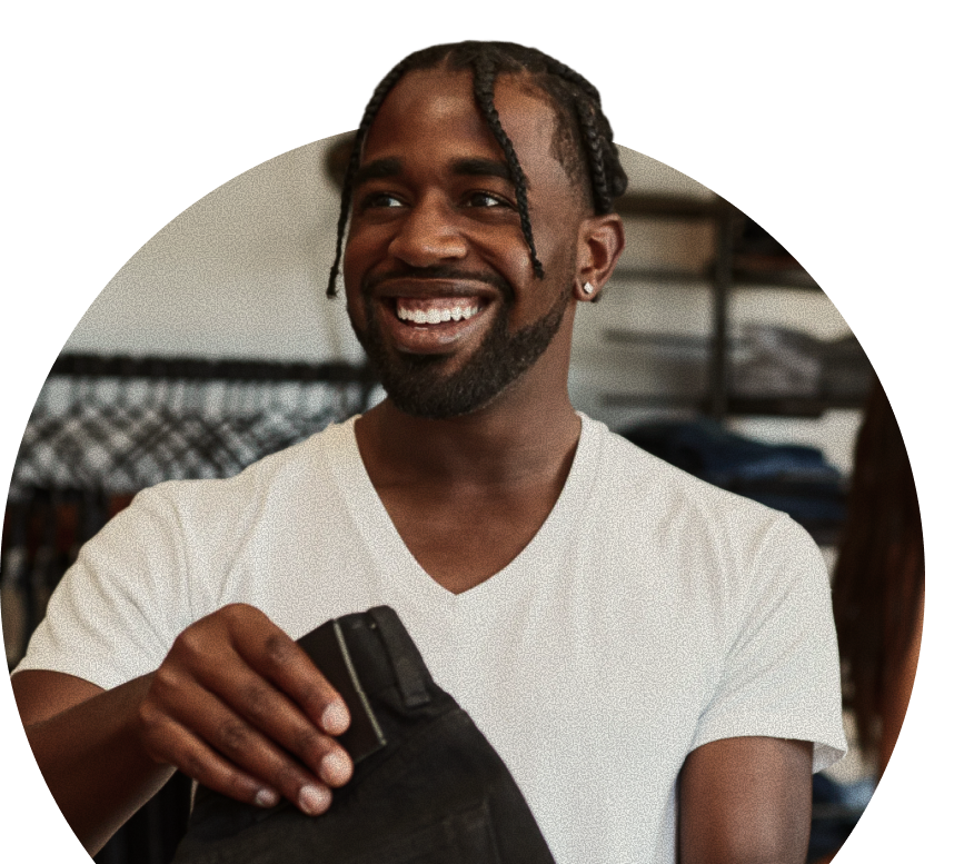 A smiling man in a white v-neck t-shirt holding a pair of black jeans.