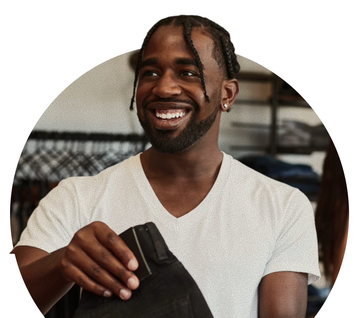 A person wearing a white t-shirt smiles while holding a pair of black pants in a clothing store.