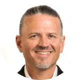 A man with short, slicked-back salt-and-pepper hair and a goatee smiling at the camera against a plain white background.
