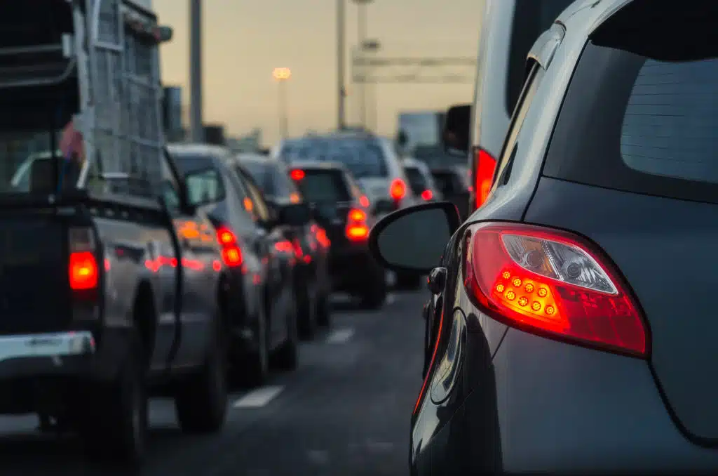 Cars are stuck in heavy traffic on a multilane road during what appears to be the evening as the sky is dimly lit.